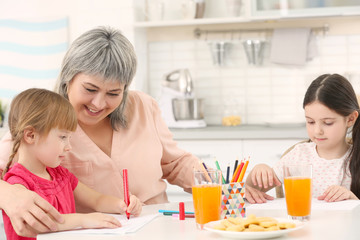 Wall Mural - Little girls with grandmother drawing at kitchen table