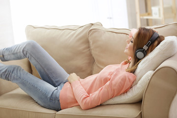 Wall Mural - Beautiful young woman listening to music while lying on sofa at home