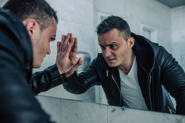 Quite wealthy man with the beaten person looks at themselves in a mirror and looks in the face. He is very angry and ready to revenge. At the man cheekbones are strained.