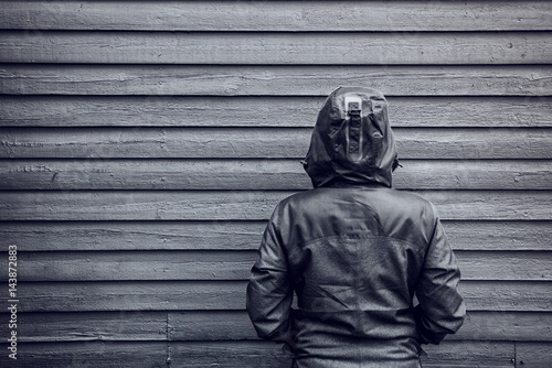 Cuadros en Lienzo Unrecognizable hooded female person facing wooden wall