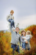 © Daria - Family mom, dad, son and daughter are walking in the high yellowed grass in the meadow. The father holds his son high above himself on one hand. Mom hugs her daughter