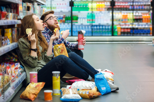 Cuadros en Lienzo Couple sitting on the supermarket floor and eating snacks