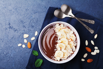 Wall Mural - Chocolate banana almond coconut smoothie bowl on stone table top view. Healthy breakfast or dessert. Flat lay.