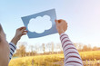 © Connect Images - Woman standing in rural setting, holding paper with cut-out of cloud, towards sky