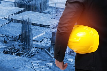 Wall Mural - businessman in suite hold in hand yellow safety helmet, industrial technology and business concept on blurred construction site workers background, color tone effect.