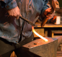 Making of horseshoe. Male worker with pliers and hammer making horseshoe.