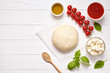 Raw pizza dough with baking ingredients: dough, mozzarella, tomatoes sauce, basil, olive oil, cheese, spices. Italian margherita preparation on white wooden table. Italian pizza margarita
