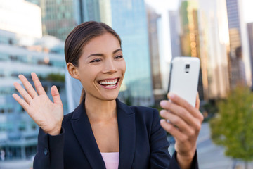 Wall Mural - Video chat business meeting concept. Businesswoman taking selfie photo using smart phone app on smartphone for social media smiling happy wearing suit jacket outdoors. Urban female professional.