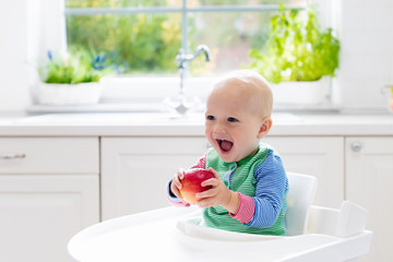 Wall Mural - Baby boy eating apple in white kitchen at home