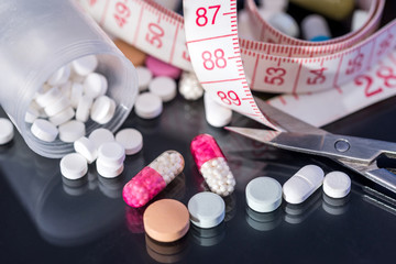 medical pills, vitamin tablets with measuring tape isolated on black background.