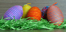Easter Multicolored Decorative Eggs With Wrapped Yarn In Green Grass Nest On Wooden Background, Close Up. Easter Concept. Homemade Decoration.  