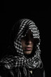hidden man with palestinian scarf over head in front of isolated black background