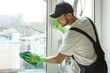 © Africa Studio - Young man cleaning window in office
