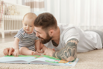handsome tattooed young man playing with cute little baby at home