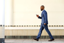 Side Portrait Of Young African Business Man Walking With Mobile Phone