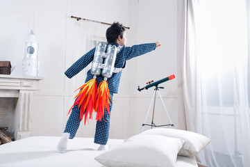 Back view of cute little boy in pajamas playing astronaut on bed