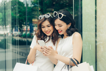 Wall Mural - Beautiful asian girls with shopping bags using smartphone at the mall