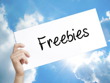 Freebies Sign On White Paper. Man Hand Holding Paper With Text. Isolated On Sky Background