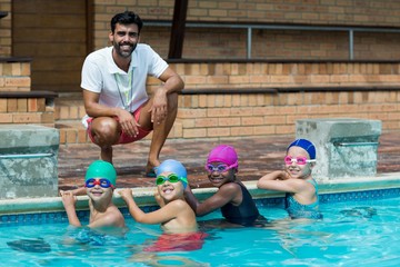 Happy male trainer with little swimmers at poolside