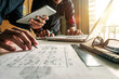 © Nuttapong punna - Two colleagues discussing data working and tablet, laptop with on on architectural project at construction site at desk in office