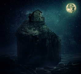 Wall Mural - Surreal image with a wood house on the top of a rock hill, near the sea, beyond the starry night sky and a young man, holding a rope, try to catch and pull the full moon.