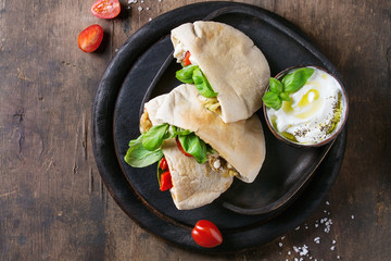 Wall Mural - Pita bread sandwiches with grilled vegetables paprika, eggplant, tomato, basil and feta cheese served on black chopping board over dark wooden background. Healthy fast food concept. Top view space