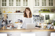© sepy - Managing her coffee shop online. Cropped shot of a female barista using a laptop in her coffee shop while standing by the counter. Small business.