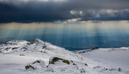 Wall Mural - Sunny spells through thunderstorm clouds on a snowy mountain top