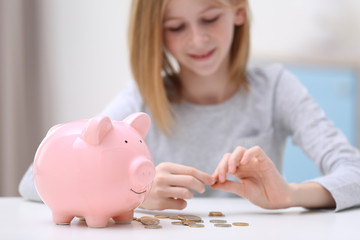 Poster - Cute girl with piggy bank and coins at home, closeup