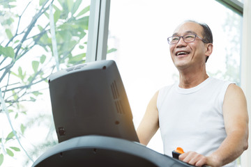 Close up Asian senior man exercising on treadmill machine with copy space. Relaxing and smiling.