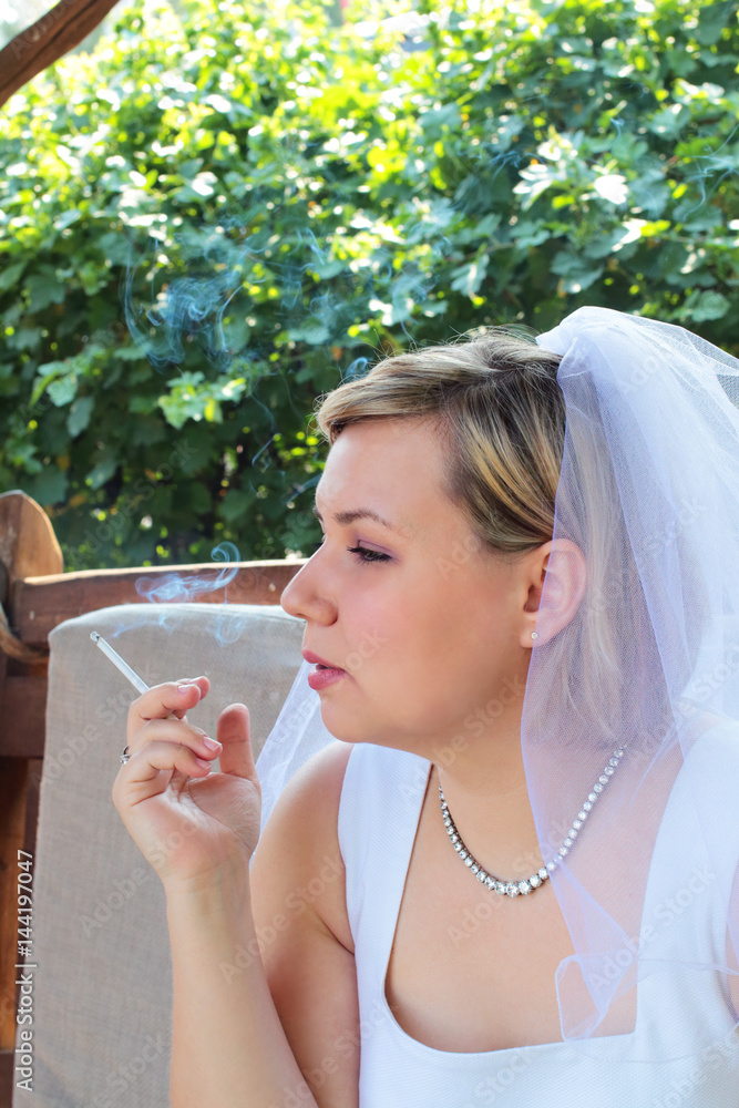 brides smoking cigarettes Young nervous sad bride in a white wedding dress smoking a cigarette  outdoors against a background of green foliage. Portrait in profile with smoke  cigarette smoked Stock-foto