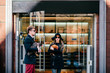 © benevolente - Man in black coat and opens door to a beautiful model long hair girl in glasses and elegant hat and fashion clothes coming out of boutique with chicken in hands after shopping. Celebrity pets concept.