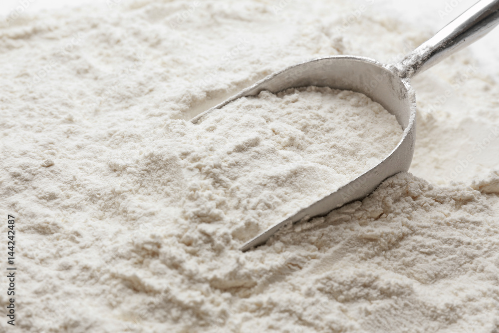 Metal scoop on sprinkled wheat flour background