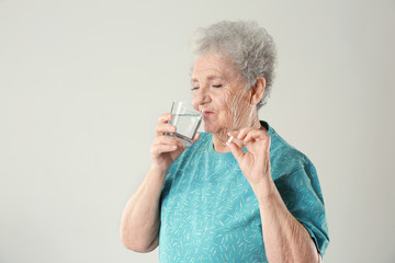 Poster - Elderly woman taking pill on light background