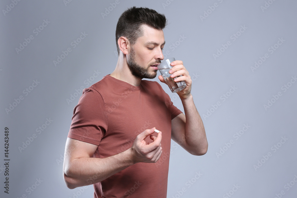 Handsome young man taking pill on color background