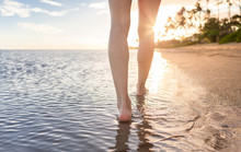 Woman's Feet Walking Along A Beautiful Beach In Hawaii At Sunset.  