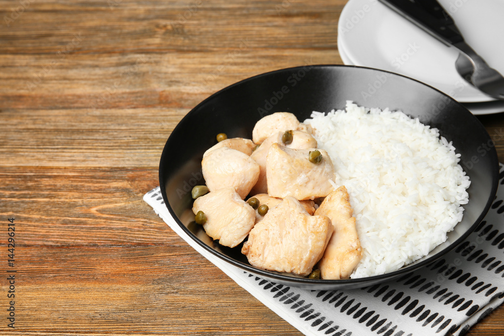 Black plate with delicious chicken and rice on wooden table