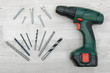 © gearstd - A green electric drill, several twisted drill bits and bolts placed on a white wood background.