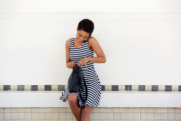 Wall Mural - Young african woman talking on mobile phone and looking in bag