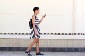 Wall Mural - side portrait of young woman walking on with cellphone and bag