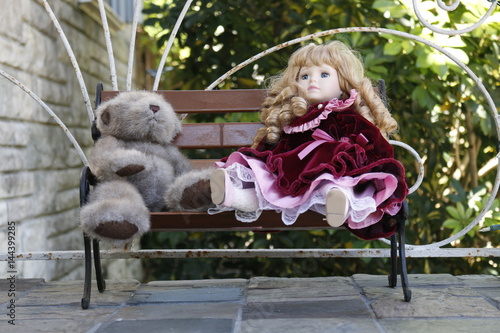Fotografie, Obraz Porcelain doll and teddy bear are sitting on the bench