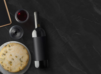 Red Wine bottle with cheese and wineglass on a black stone background with copy space. Wine bottle mockup. Top view.