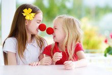 Happy Little Sisters Wearing Red Clown Noses Having Fun Together On Sunny Summer Day At Home
