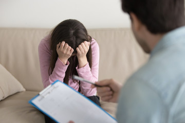 Wall Mural - Young woman at the psychologist, feeling hopeless and depressed, crying holding her head in hands, upset teenage girl just found out about unwilling pregnancy or having disease