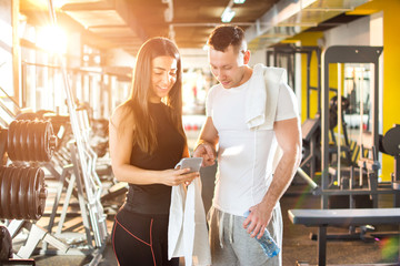 Wall Mural - Handsome guy showing something on a smartphone to his female friend at gym.