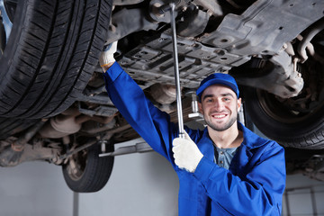 Wall Mural - Young mechanic fixing wheel under car in  service