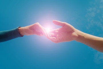 Female and male hands reaching to each other on sky background. Help and care concept