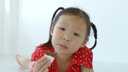 Wall Mural - little asian girl eating chocolate bar on the floor