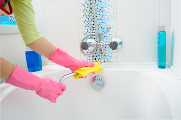 Wall Mural - A woman cleaning bath at home. Female washing bathtub and faucet