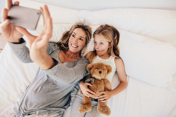 Wall Mural - Mother and daughter lying on bed and taking selfie